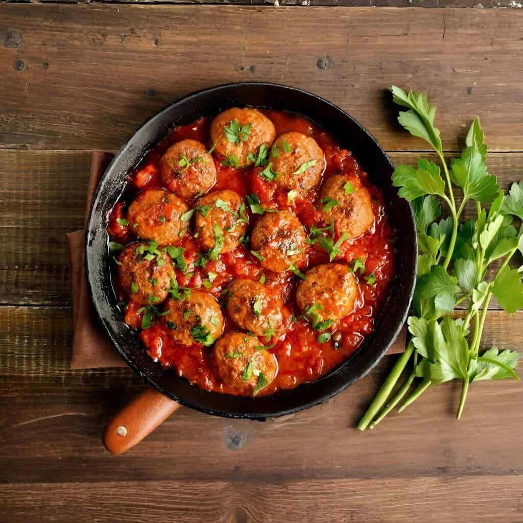 Beef meatballs in tomato sauce with fresh herbs in a black skillet.