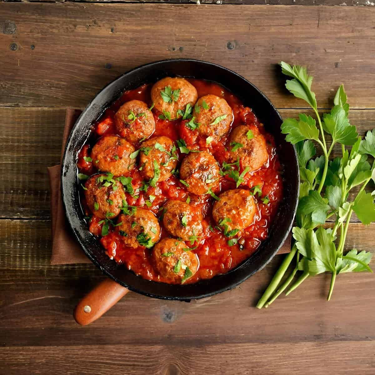 Beef meatballs in tomato sauce with fresh herbs in a black skillet.